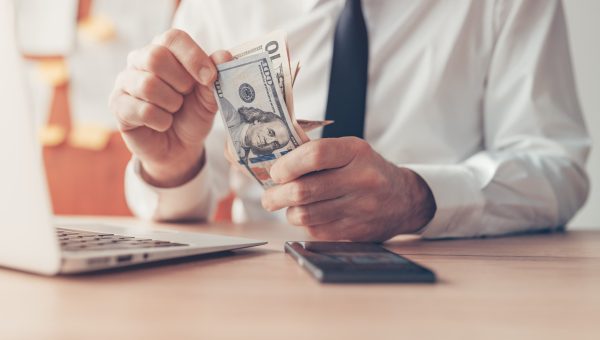 Business revenue, businessman counting US dollar cash money in office, close up with selective focus