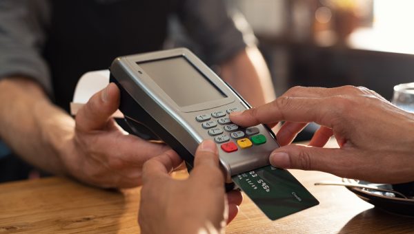 Closeup of hand using credit card swiping machine to pay. Female hand with credit card paying through terminal for payment in coffee shop. Woman entering debit card code in swipe machine.