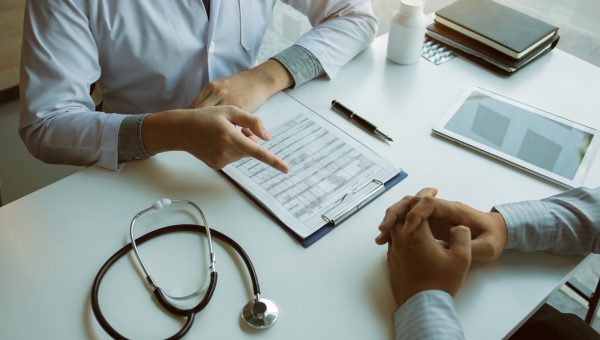 Male patient listening to doctor at desk and consulting with healthcare in hospital.