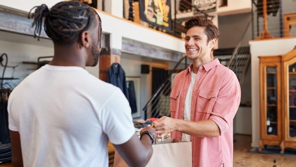 Sales Assistant Handing Purchases To Male Customer In Fashion Store