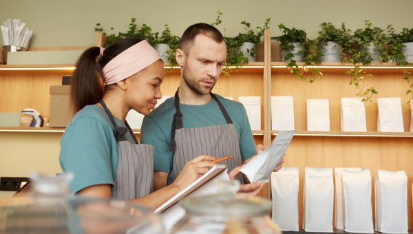 Waist up portrait of two young waiters wearing aprons while doing inventory in cafe or coffee shop, copy space