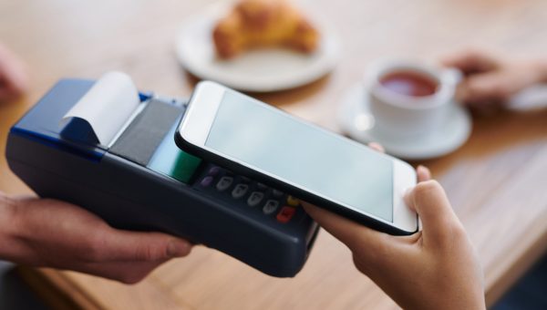 Close-up of unrecognizable woman putting smartphone to payment terminal while using contactless payment in cafe